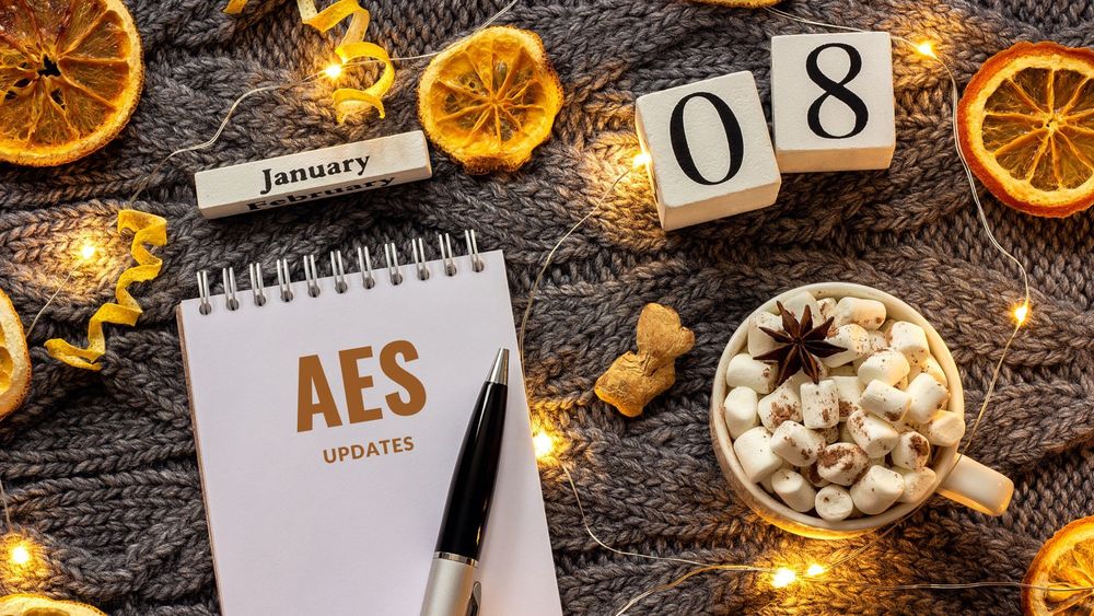 image of a notepad, pen, hot chocolate with marshmallows and dried oranges with text of AES updates, January 08